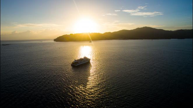 seychelles yacht from behind in sunset with island in the distance