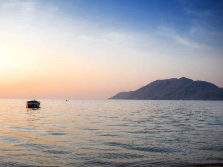 malawi local boat on the calm waters with mountain backdrops
